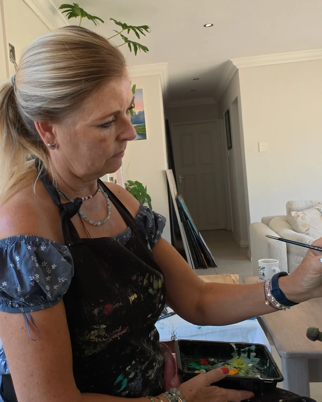 Linda painting, her brush raised to the canvas.