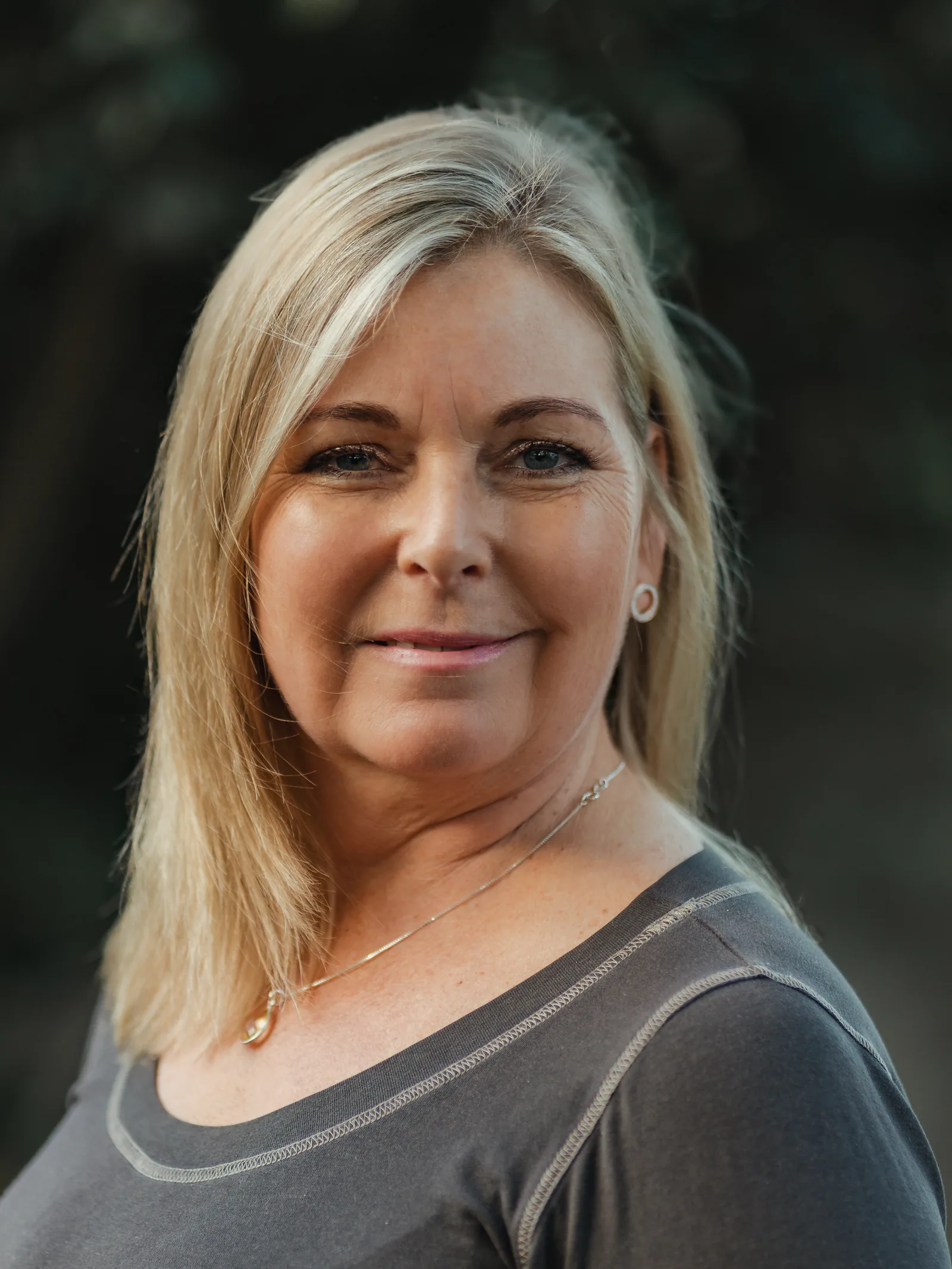 Linda Wolf, painter, smiling in a grey top, photographed outdoors in soft light.