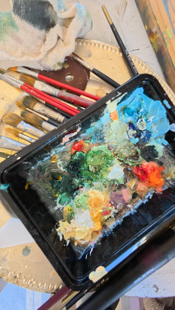 A palette tray of mixed oil colour beside a jar of brushes.